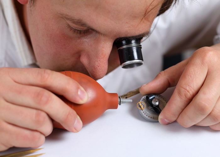 watchmaker in workshop using a loupe to see the parts to blow with air in order to clean.